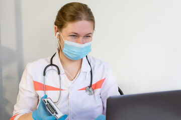 A female nurse, wearing a protective mask and blue medical gloves, works at a laptop, she enters the patient's data.