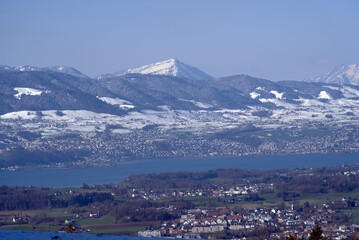 Panoramic landscape with lake Zurich and snow capped Swiss alps in the background. Photo taken April 8th, 2021, Zurich, Switzerland.