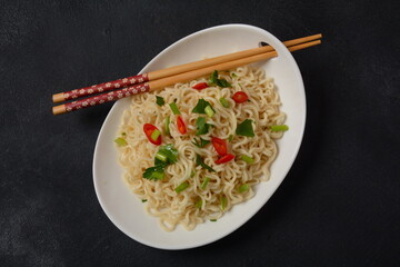 Bowl of instant noodles with chopsticks on black background.