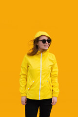 Attractive girl in sunglasses and a yellow raincoat isolated on a yellow background