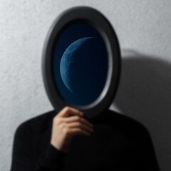 Half moon inside of mirror black frame in hands of man on textured grey background. Contemporary...
