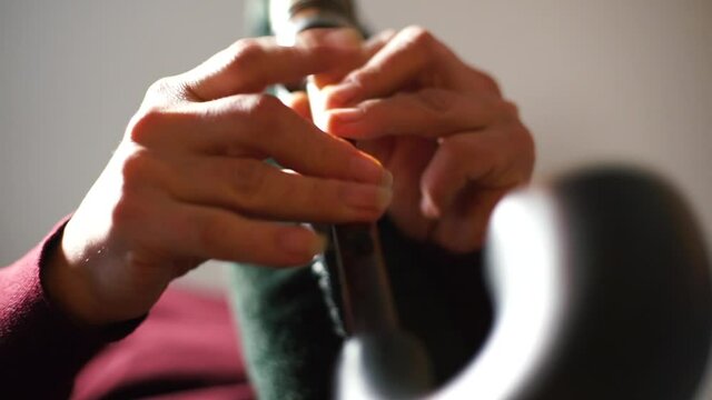 The musician's hands expressively make a melody on the pipe. Fast fingers close holes, making music. Camera movement.