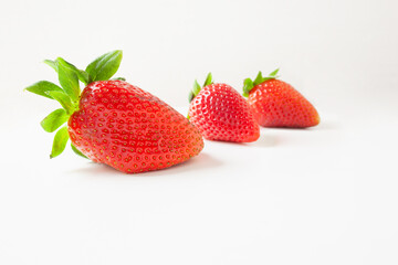 Three strawberries with green leaves stacked diagonally on white background