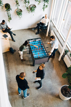 Male and female colleagues playing foosball while taking break from work in office