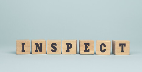 The word INSPECT made from wooden cubes on blue background