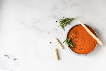 Tomato soup garnish with ground pepper, rosemary and bread sticks, light background. Top view. Copy space.