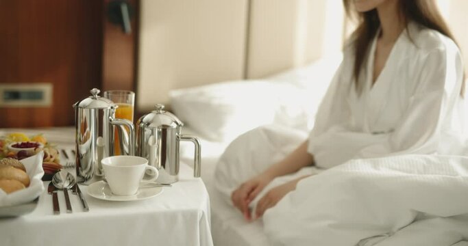 Asian girl pouring fresh coffee from pot in cup, having luxury healthy breakfast in hotel room in morning - hotel catering service 4k footage
