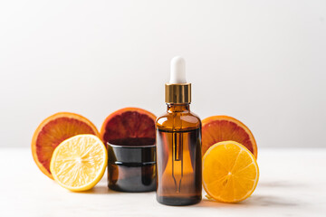 Serum in glass bottle with pipette on the background of slices of orange and lemon. Cosmetic product in  bottle with vitamin C