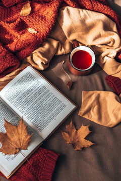 Hot cup of tea with autumn leaves and light garland decor on brown plaid in bed. Comfort and relaxation concept, vertical photo orientation. Flat lay style