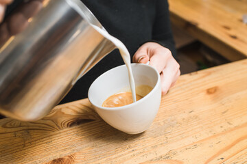Woman barista makes coffee, pours milk into cappuccino coffee