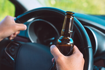 Closeup of drunk driver hands on the steering wheel with a bottle of beer. Driving under alcohol...
