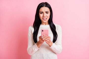 Photo of nervous troubled lady hold telephone look screen bite lip wear white pullover isolated pink color background