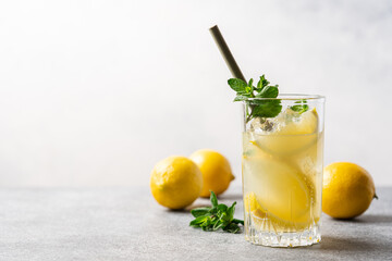 Citrus lemonade with mint and ice in glass with bamboo tube. Refreshing summer drink. White background, side view, close-up view