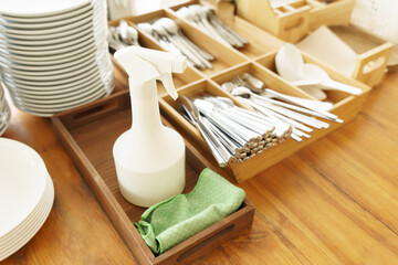 Stainless steel cutlery spoon, forks, knives and dished well organized on a self service station in a cafe or restaurant with 70% alcohol spray to clean the table. Covid 19 pandemic new normal. 