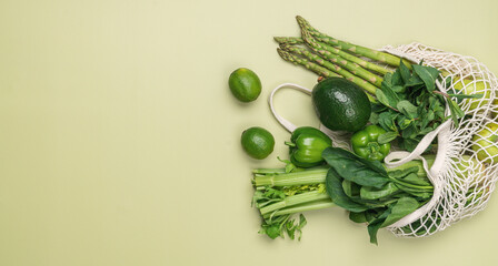 Green vegetables and fruits in mesh bag on pastel green background. Local, farm, organic food. Plastic-free shopping