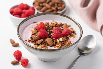 Raspberry yogurt in bowl with granola and almond nuts. Delicious healthy breakfast on white...