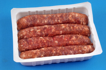 Barquette en plastique de saucisses de porc crues en gros plan sur fond bleu