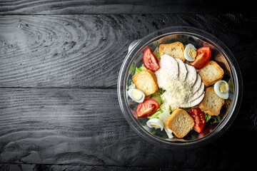 Healthy caesar salad in plastic package for take away or food delivery on black background. banner, menu recipe place for text, top view