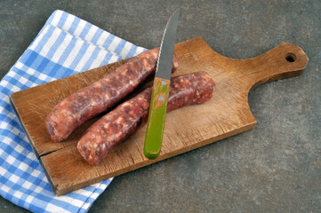 Saucisses de porc crues sur une planche à découper avec un couteau et un torchon à carreaux en gros plan sur fond gris