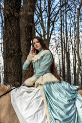 Fototapeta premium beautiful woman in blue suit with light brown horse in spring forest 