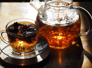 Glass teapot and glass with brewed tea in the evening light. Herbal medicinal tea with dried flowers of marigold and calendula.
