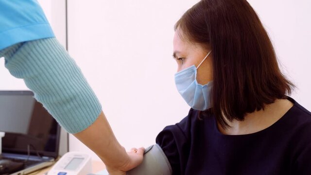 A nurse measures the arterial blood pressure of a woman with a mask on her face. Examination before vaccination against coronavirus.