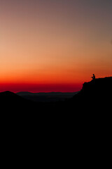 Red sunset with mountain silhouette. A man on mountain in sunset. Traveler on rock waving hands.
