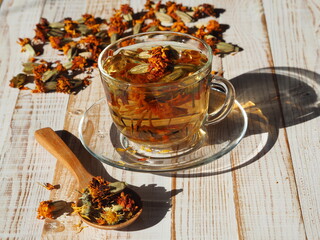 Evening light with long shadows falls on a cup of herbal medicinal tea with dried flowers of marigold.