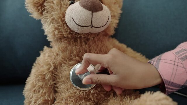 Hand of child playing doctor with teddy bear, examining toy with stethoscope
