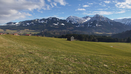 Fototapeta premium Winteruntypisches Bergpanorama in den Allgäuer Alpen mit grünen Talflanken und Schnee nur auf den Gipfeln
