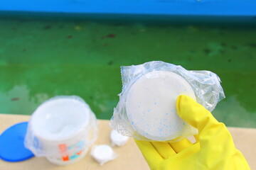 White chlorine tablet in the hand of maintenance personnel for disinfection of swimming pools. Water purification. Green water with bacteria in the pool in the spring. Preparation for swimming.