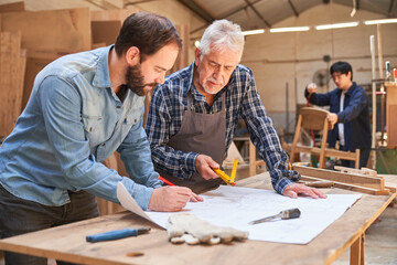 Senior craftsman and apprentice look at construction plan - obrazy, fototapety, plakaty