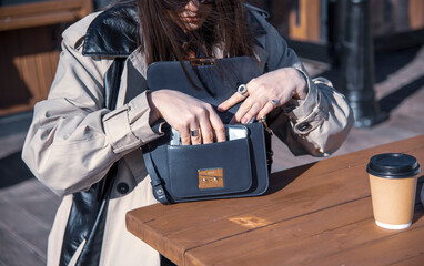 A woman in a light raincoat puts her phone in her purse.