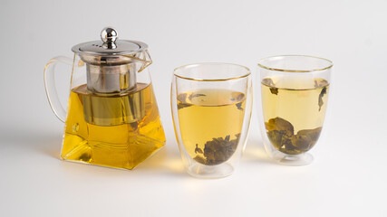 Teapot with brewed green tea and two clear glass cups. Tea leaves in a transparent pot