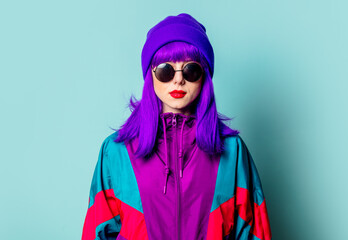 Stylish white girl with purple hair, 80s tracksuit and sunglasses on blue background