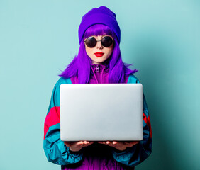 Stylish white girl with purple hair and 80s tracksuit with laptop on blue background