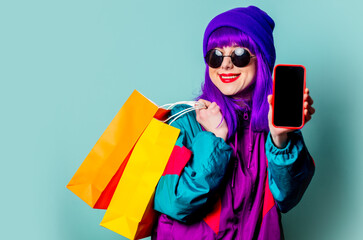 Stylish shopaholic girl in 80s tracksuit and sunglasses hold shopping bags and mobile phone - obrazy, fototapety, plakaty