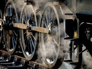 Close up of steam locomotive drive wheels and steam