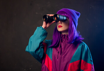 Stylish girl in 80s tracksuit with binoculars on dark background