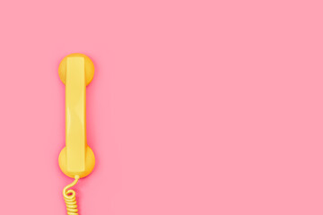 Tubo de teléfono antiguo con cable de color amarillo sobre un fondo rosa liso y aislado. Vista superior. Copy space