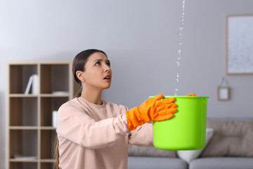Young woman collecting leaking water from ceiling at home. Time to call roof repair service