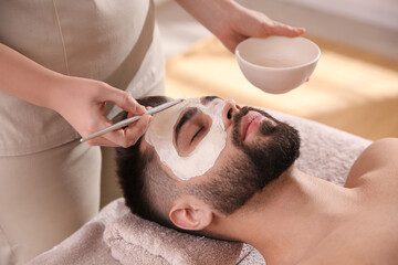 Obraz na płótnie Canvas Cosmetologist applying mask on man's face in spa salon