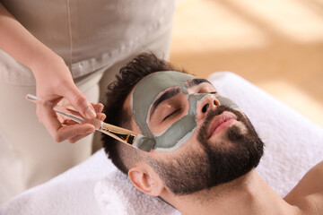 Cosmetologist applying mask on man's face in spa salon