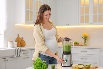 Young pregnant woman preparing smoothie at table in kitchen. Healthy eating