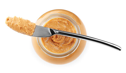 Glass jar and knife with tasty peanut butter on white background, top view
