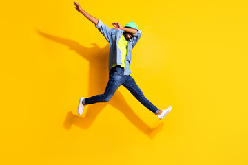 Full size profile photo of optimistic nice brunet man jump wear jacket cap jeans isolated on yellow color background