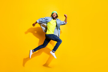 Fototapeta na wymiar Full size profile photo of optimistic nice brunet man jump wear jacket cap jeans isolated on yellow color background