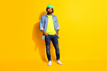Full size photo of optimistic nice brunet man wear jacket cap jeans isolated on yellow color...