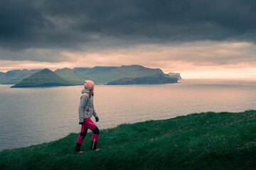Fototapeta na wymiar Woman hiking on Kalsoy Island during sunset, coast of island Eysturoy ion background, dramatic sky, Faroe Islands.