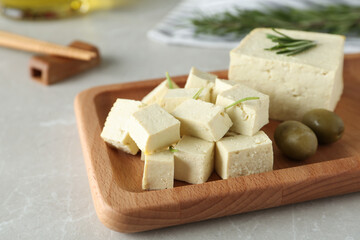 Pieces of delicious tofu with rosemary and olives on grey table, closeup. Soybean curd